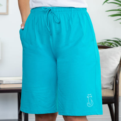 Teal shorts with a small white embroidered cat silhouette on the left leg, on a neutral background
