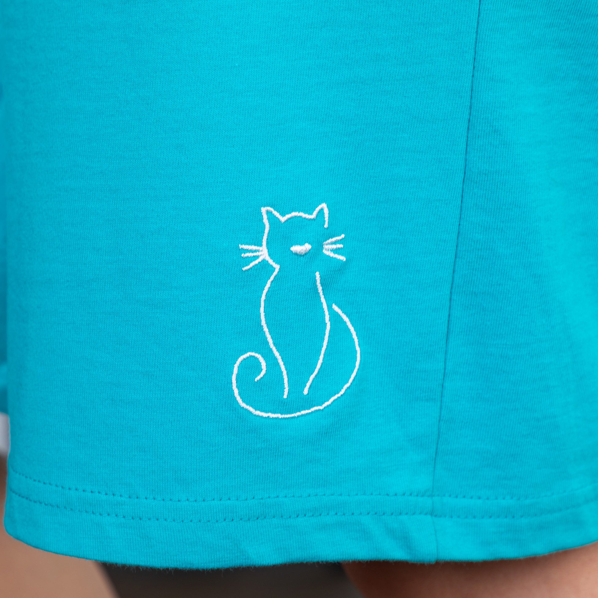 Close-up of teal shorts with a white cat embroidery.