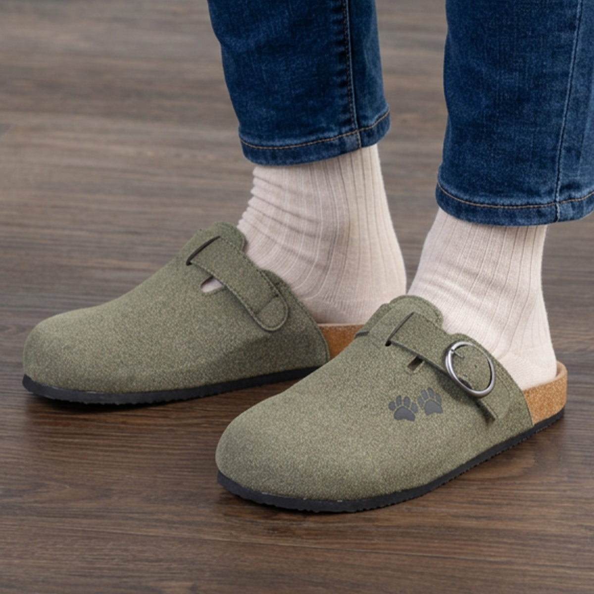 A person wearing olive green clogs with beige socks, standing on wooden floors.