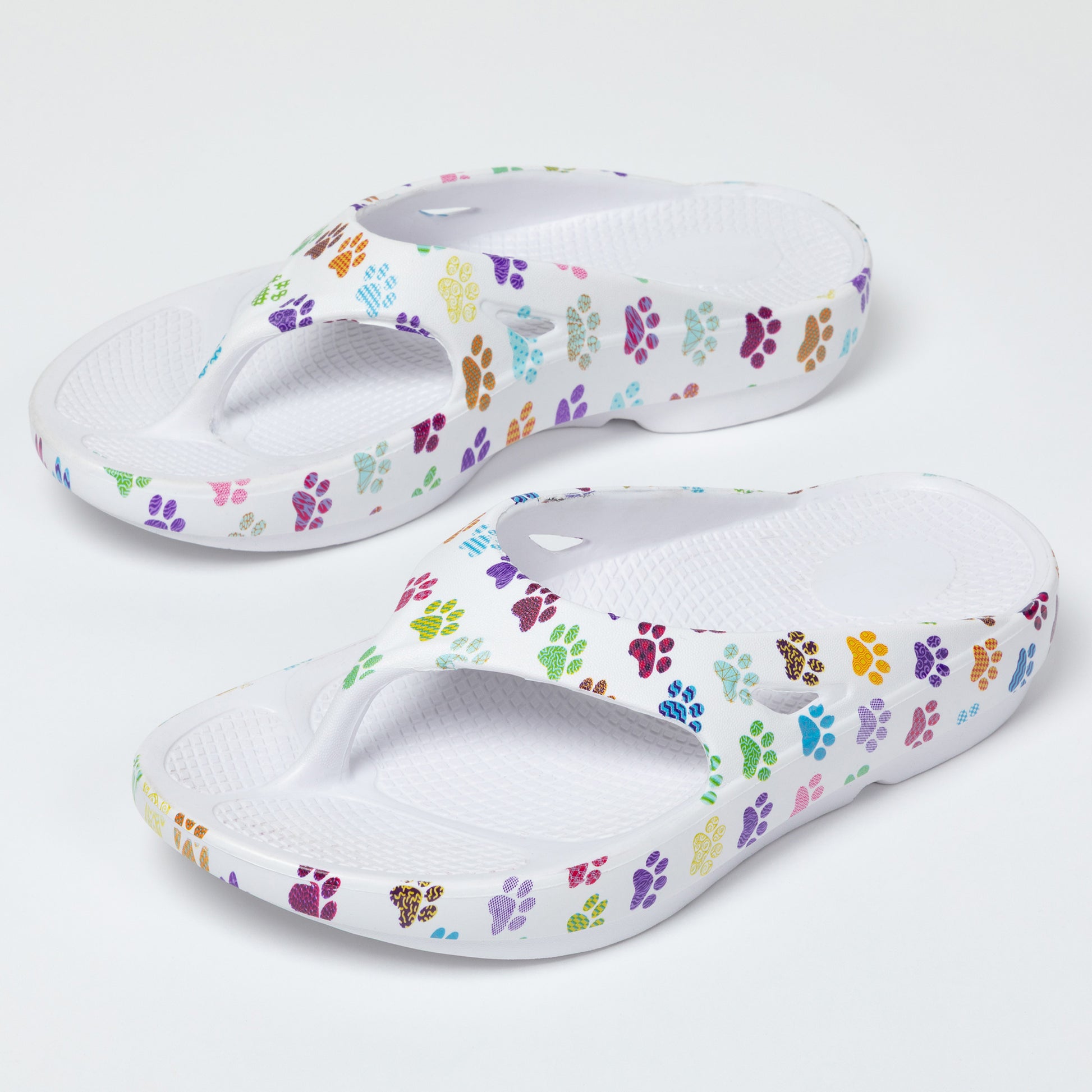 Pair of white sandals with colorful paw print pattern on a white background