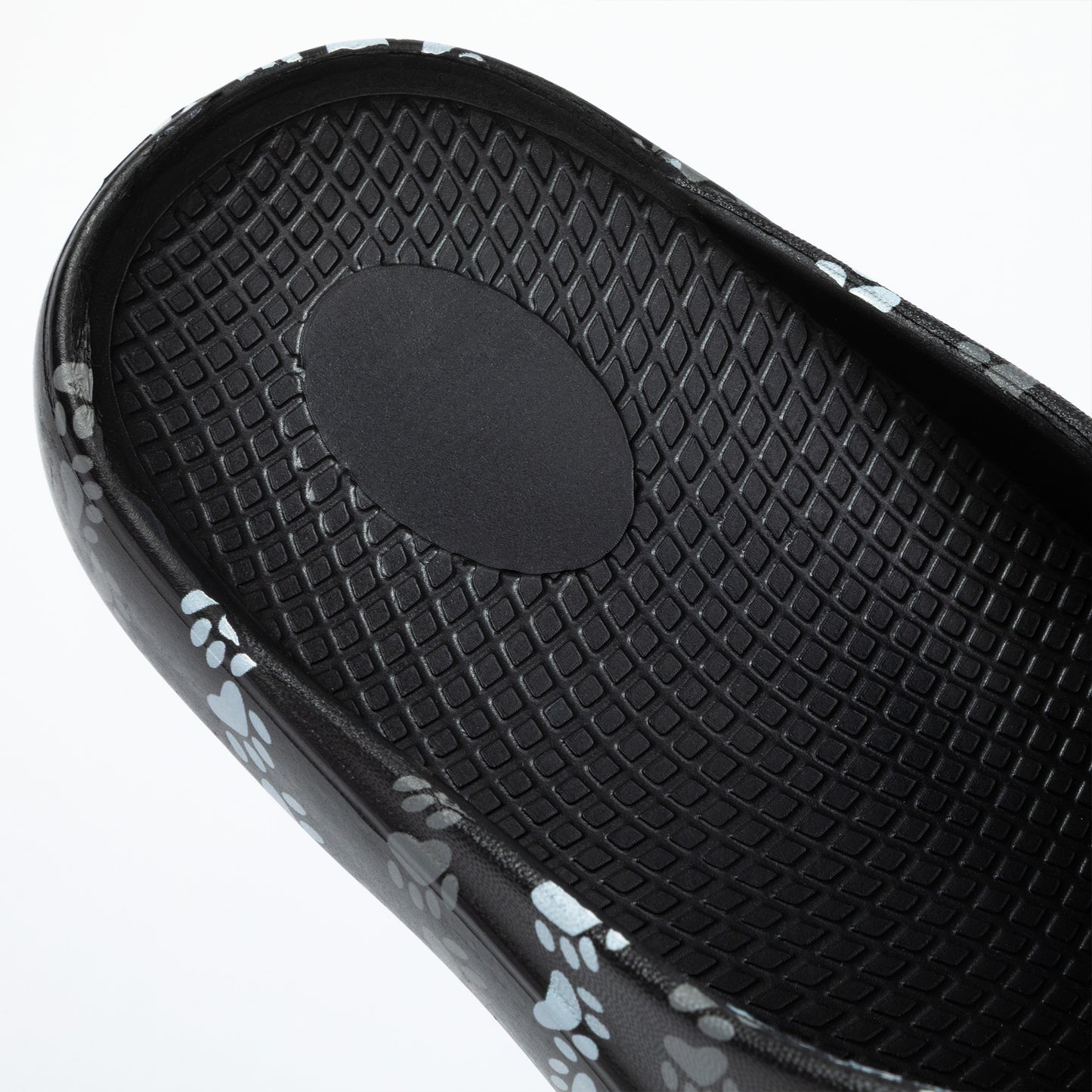 Close-up of a black sandal with textured insole and paw print pattern on a white background