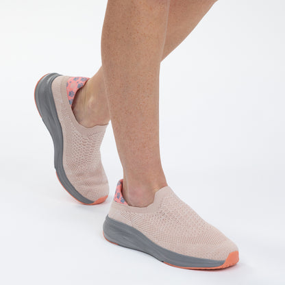 Beige slip-on shoes with gray soles worn by a person on a white background