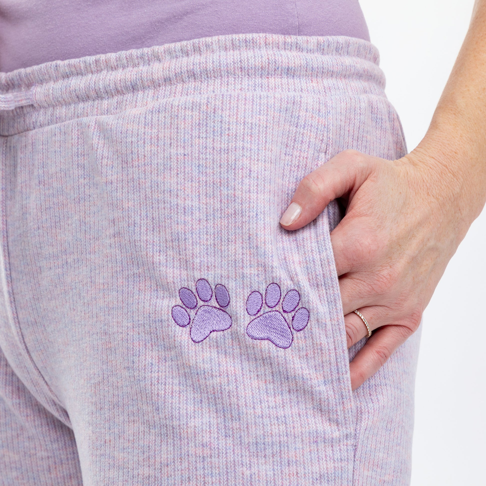 Close up of embroidered purple paw prints on the left leg of purple melange rib knit pants.