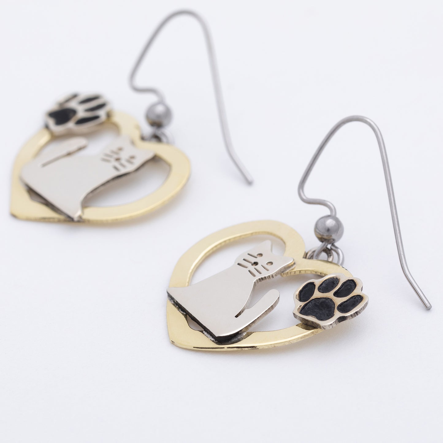 Heart-shaped brass earrings with paw prints and cats on a white background.