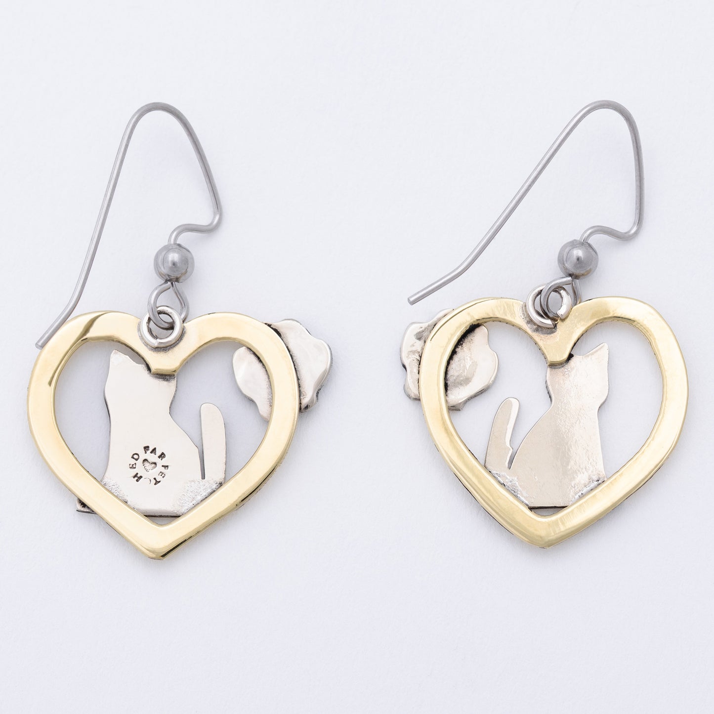 The back of heart-shaped earrings with cut-out designs of a paw and a cat on a light gray background.