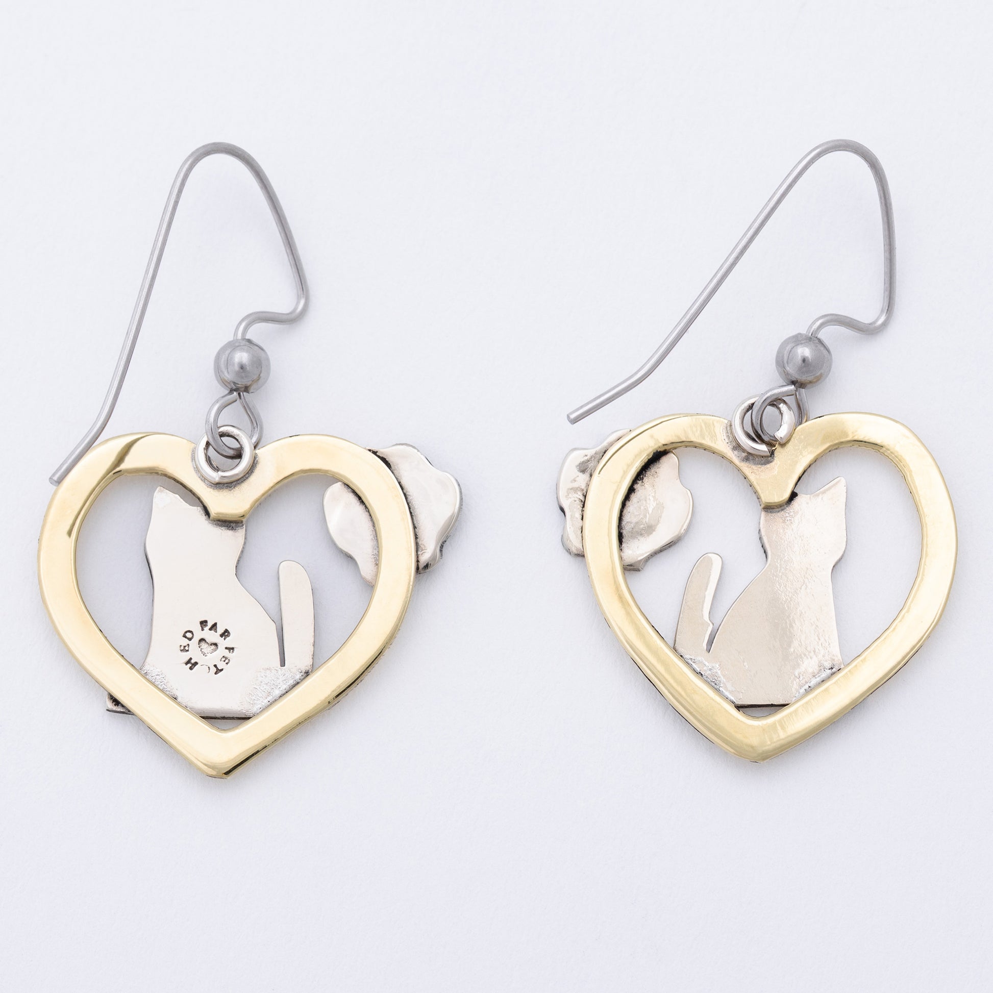 The back of heart-shaped earrings with cut-out designs of a paw and a cat on a light gray background.