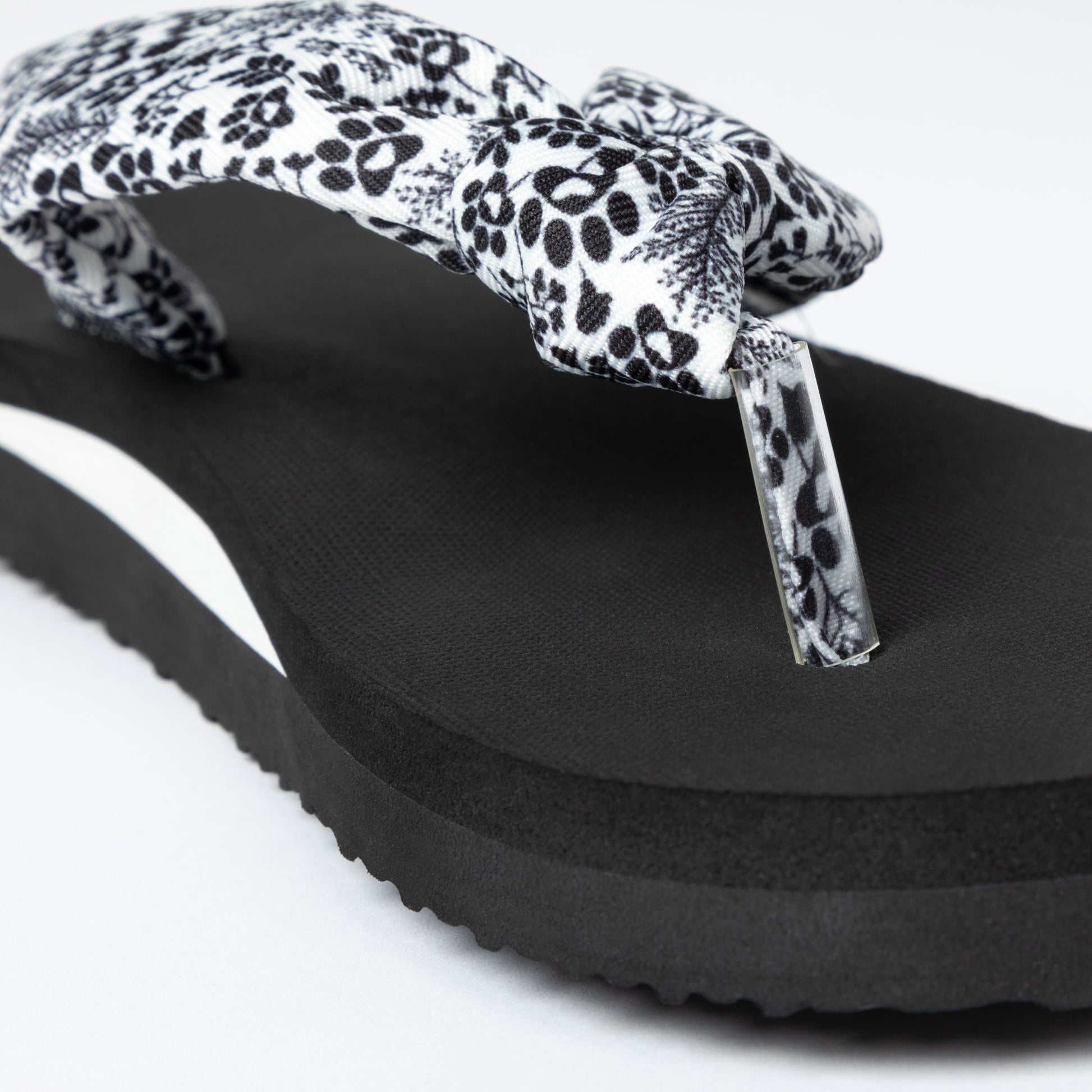 Black sandal with a floral and paw print strap on a white background