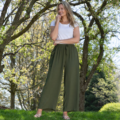 Woman wearing a white top and green wide-leg pants standing in a park.