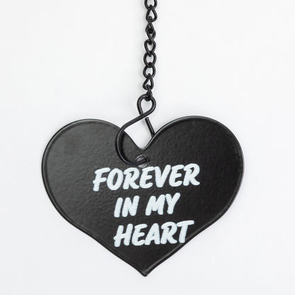 A black heart-shaped pendant with the words 'FOREVER IN MY HEART' in white lettering, suspended from a black chain against a plain white background.