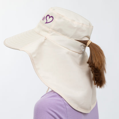 Beige sun hat with a heart logo worn by a person with a ponytail on a white background