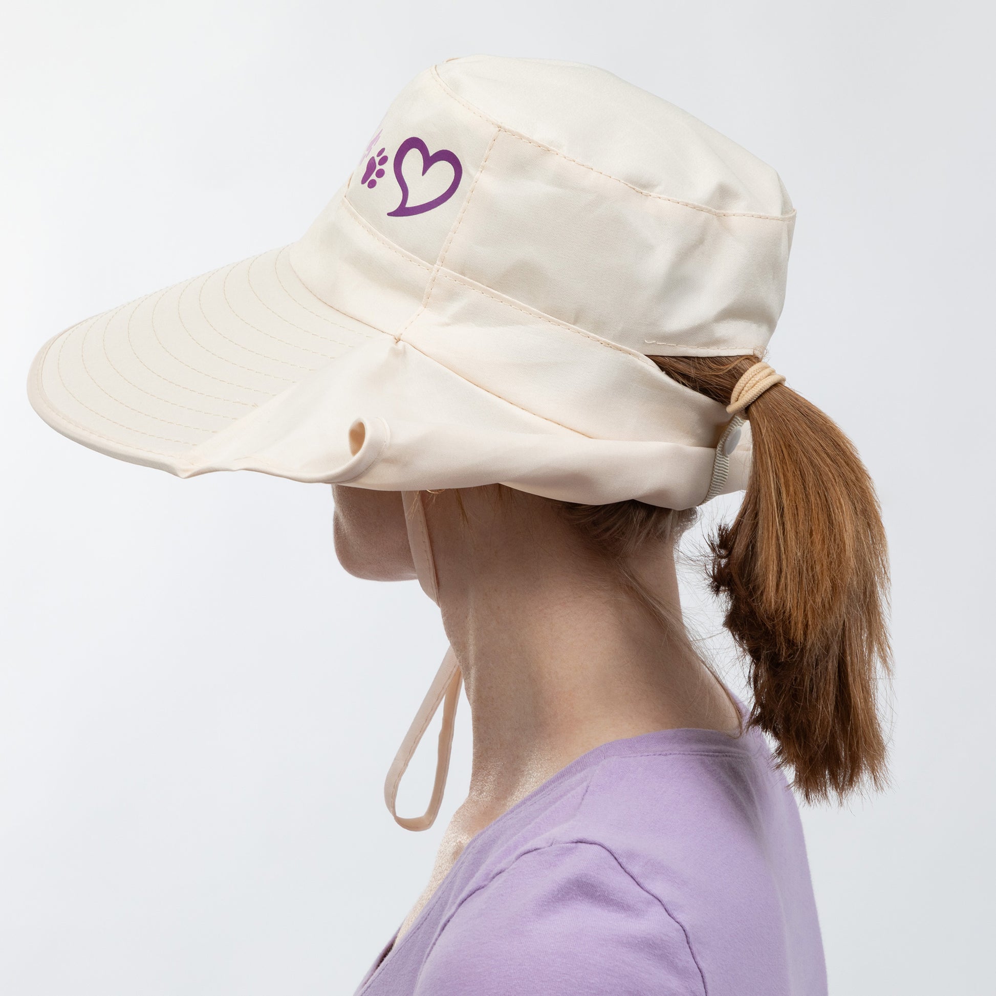 Person wearing a beige sun hat with a purple heart and paw print design on a white background.