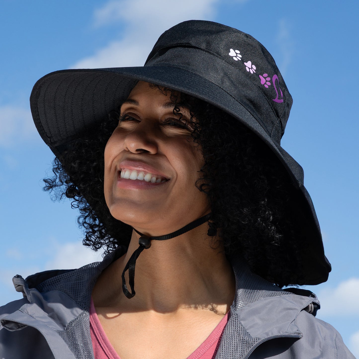 Woman wearing a black sun hat with paw prints against a blue sky.