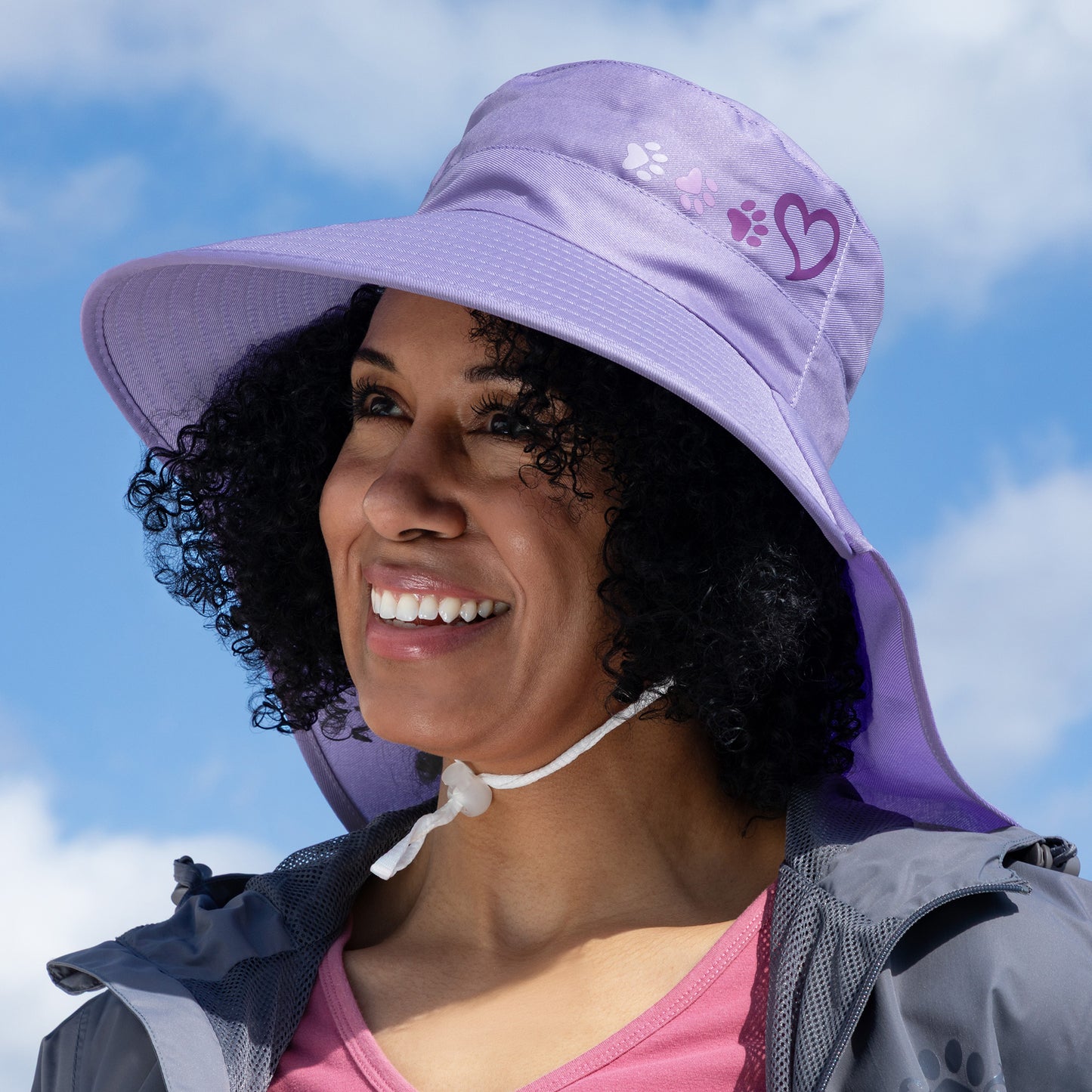 Woman wearing a purple bucket hat with a heart and paw prints design, smiling outdoors.