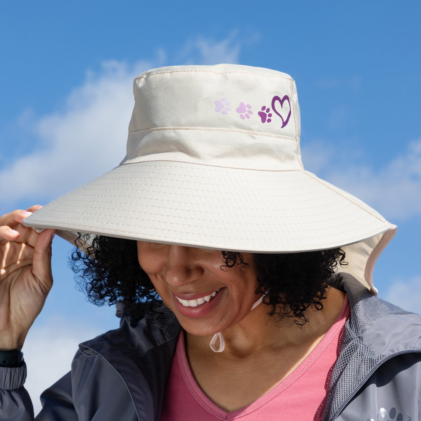 Person wearing a wide-brimmed beige hat with paw prints against a blue sky.