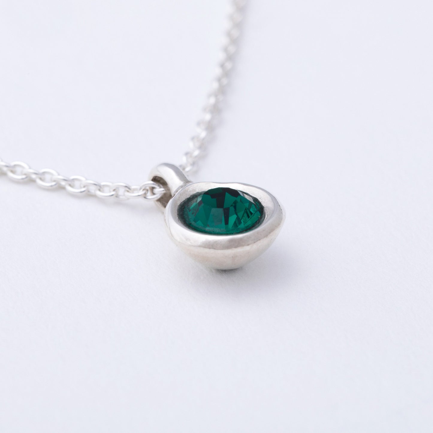 Silver necklace with a green gemstone pendant on a white background