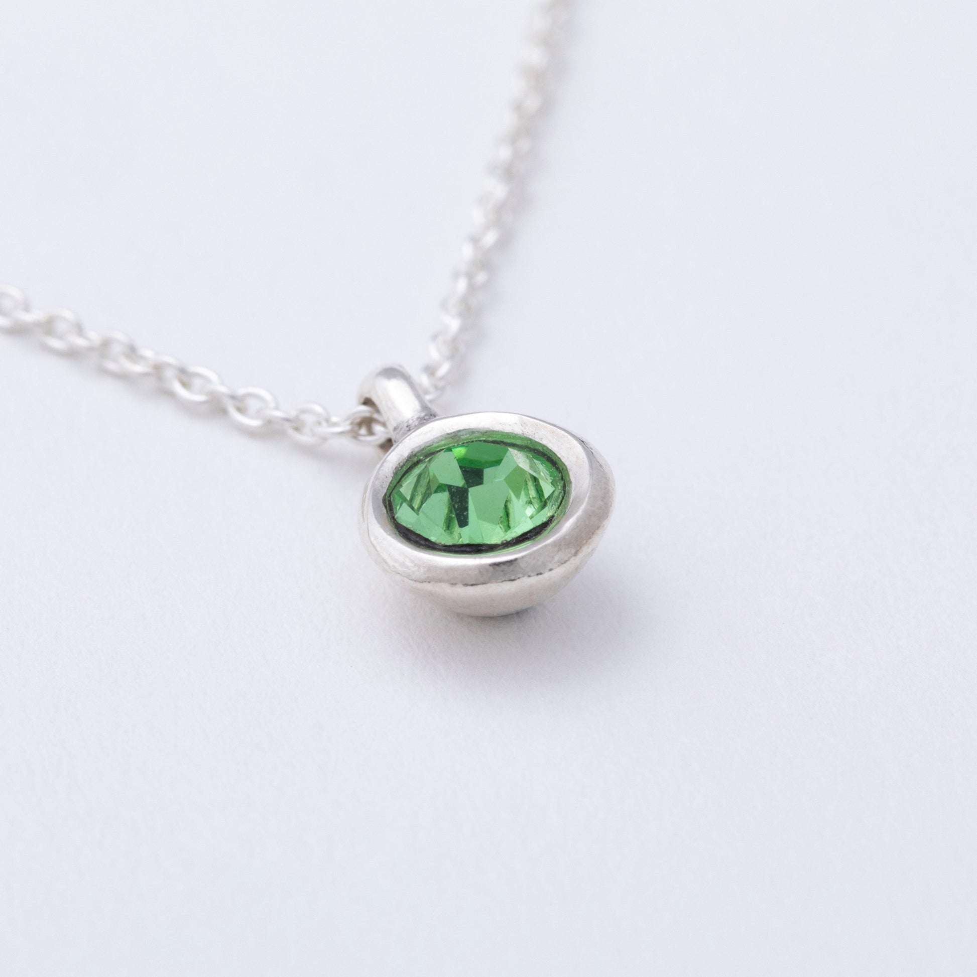 Silver necklace with a green gemstone pendant on a white background