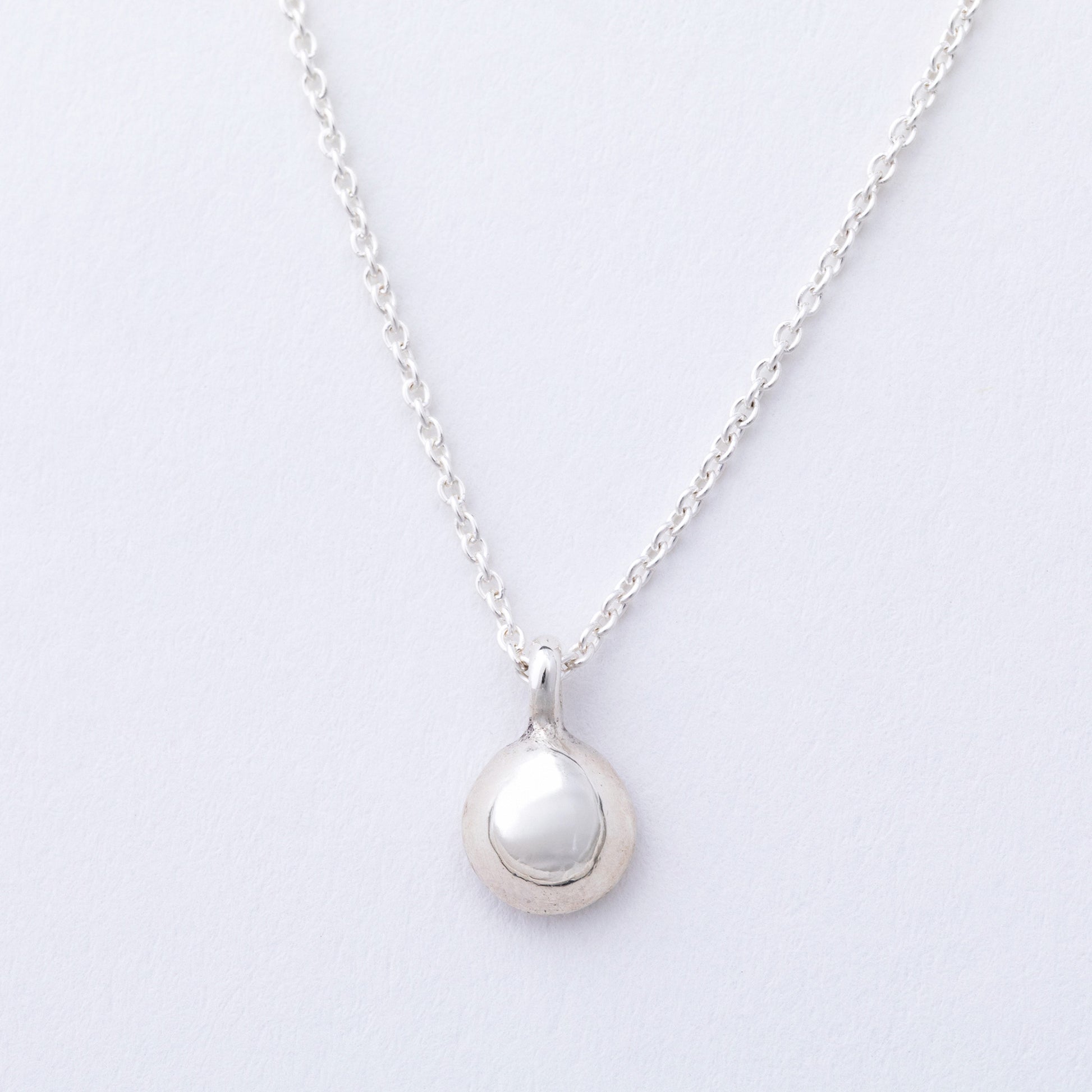 Silver necklace with a round pendant on a light gray background
