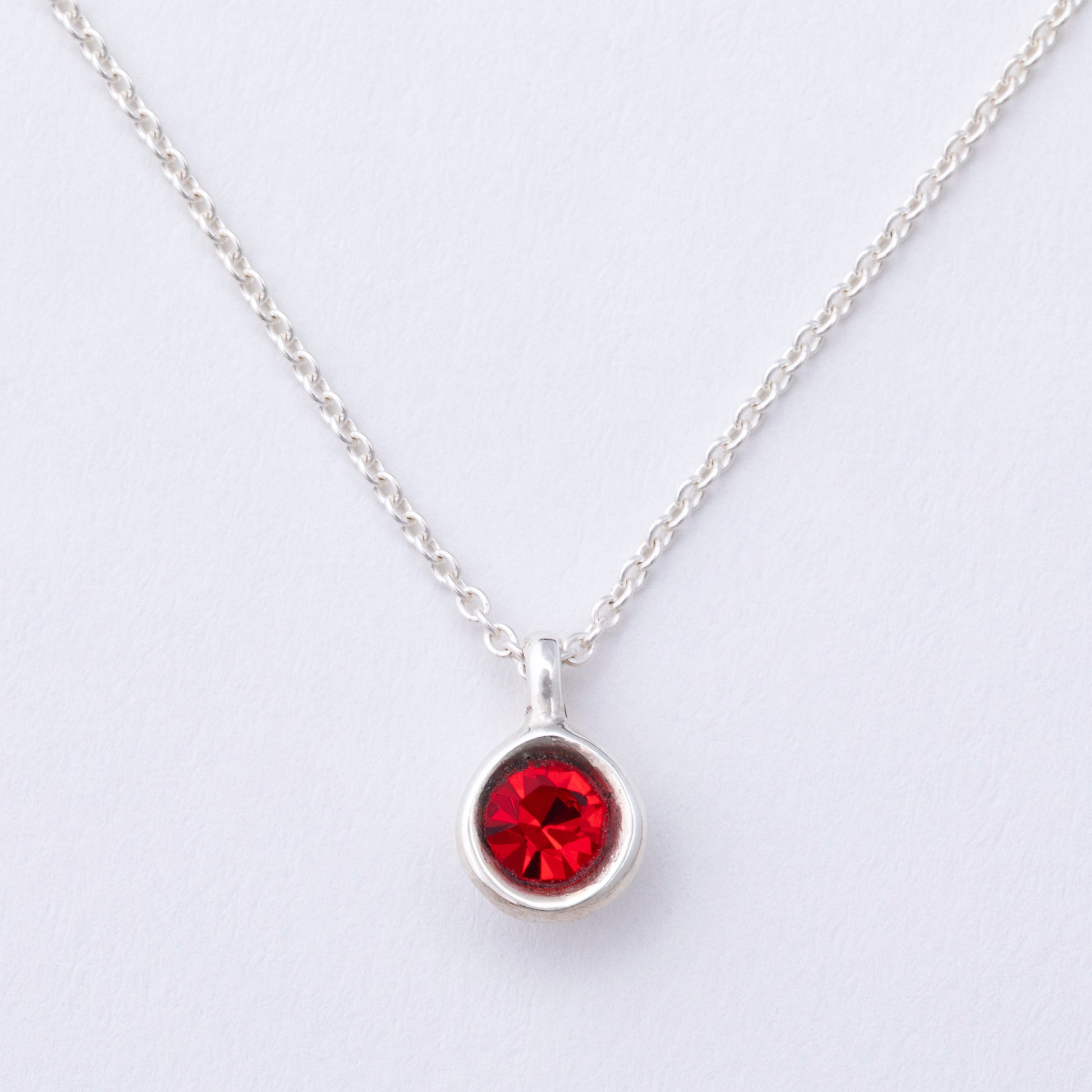 Silver necklace with a red gemstone pendant on a light gray background