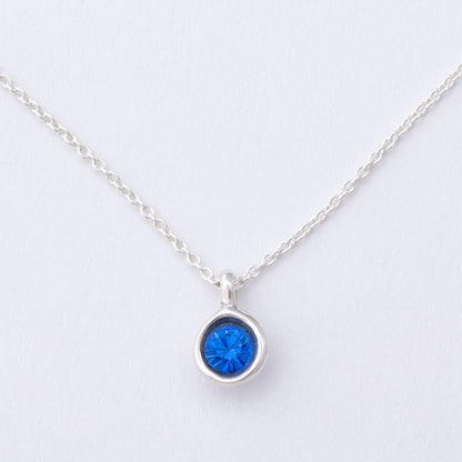 Silver necklace with a blue gemstone pendant on a light gray background