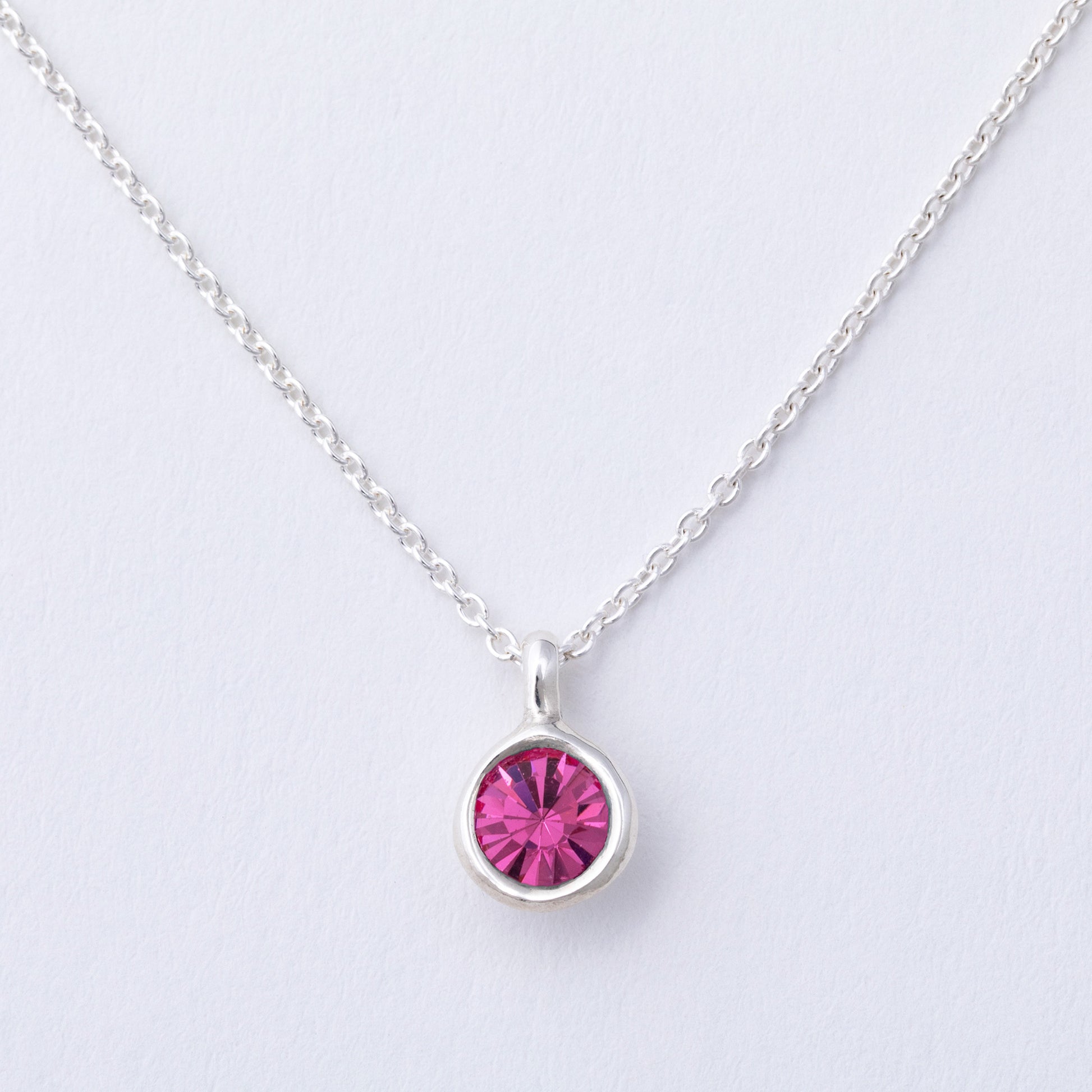 Silver necklace with a pink gemstone on a light gray background