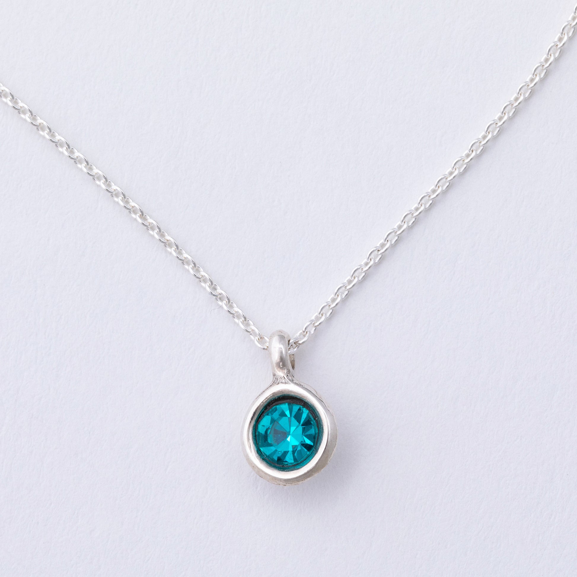 Silver necklace with a blue gemstone pendant on a light gray background