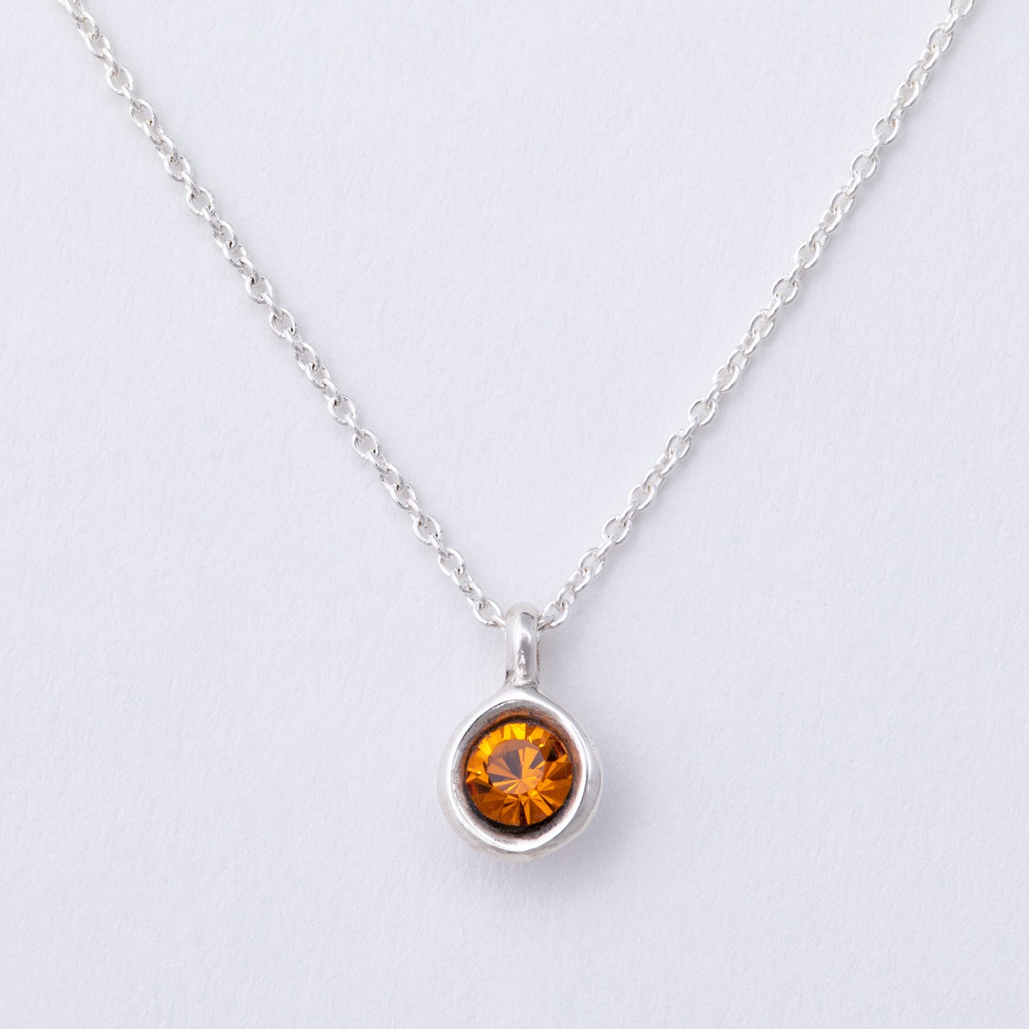 Silver necklace with a round amber-colored gemstone on a light gray background