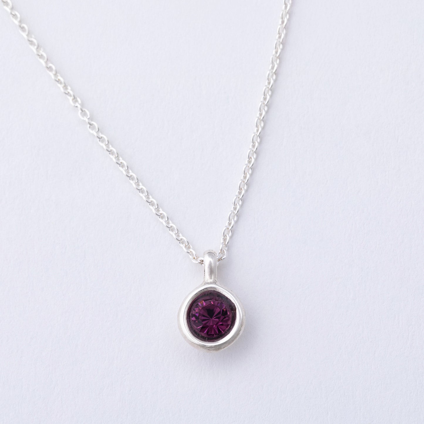 Silver necklace with a purple gemstone pendant on a light gray background