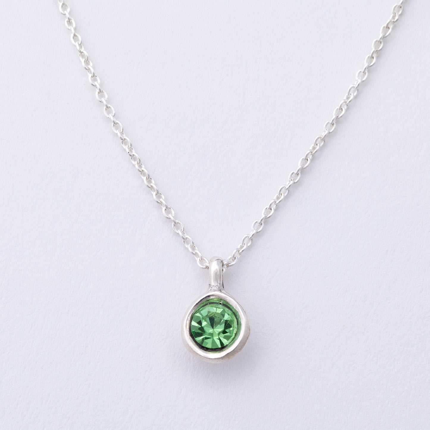 Silver necklace with a green gemstone pendant on a light gray background