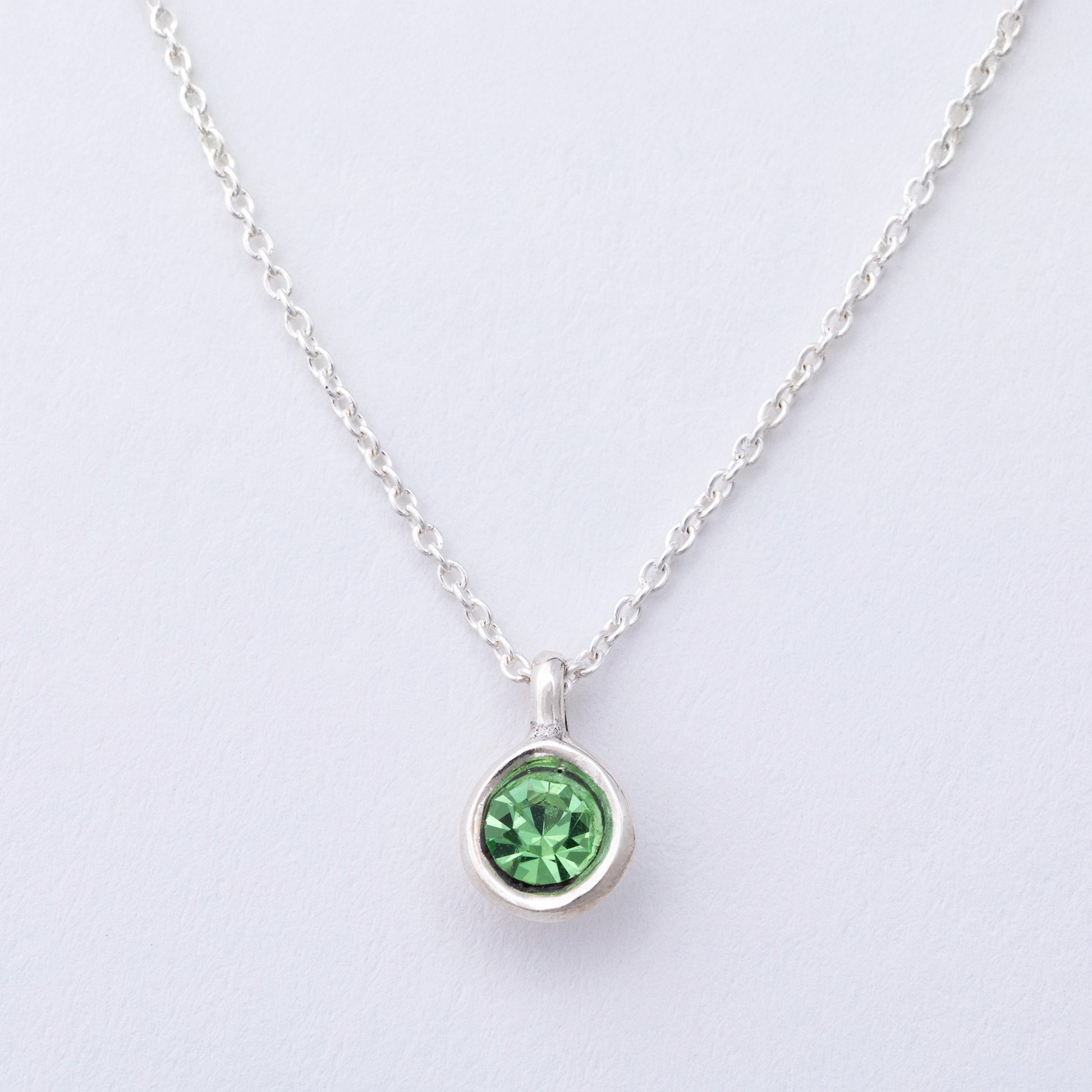 Silver necklace with a green gemstone pendant on a light gray background