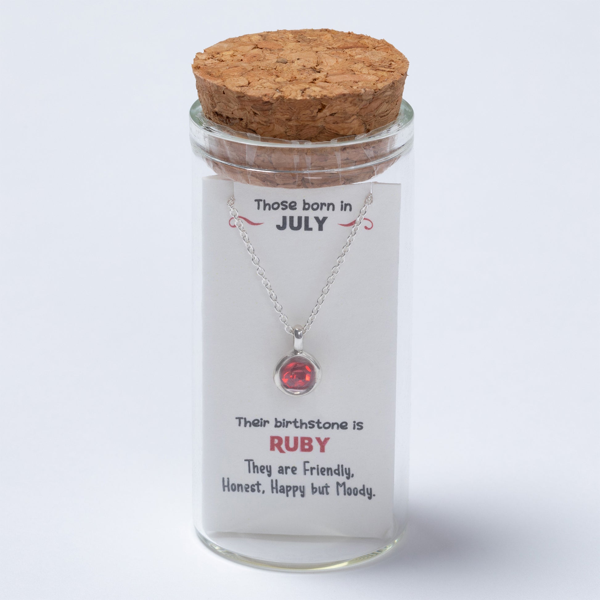 Necklace with a red gemstone in a glass jar with a cork lid, featuring text about July-born individuals and their birthstone.