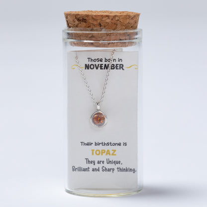 Necklace in a glass jar with cork lid, featuring text about November birthstones on a white background
