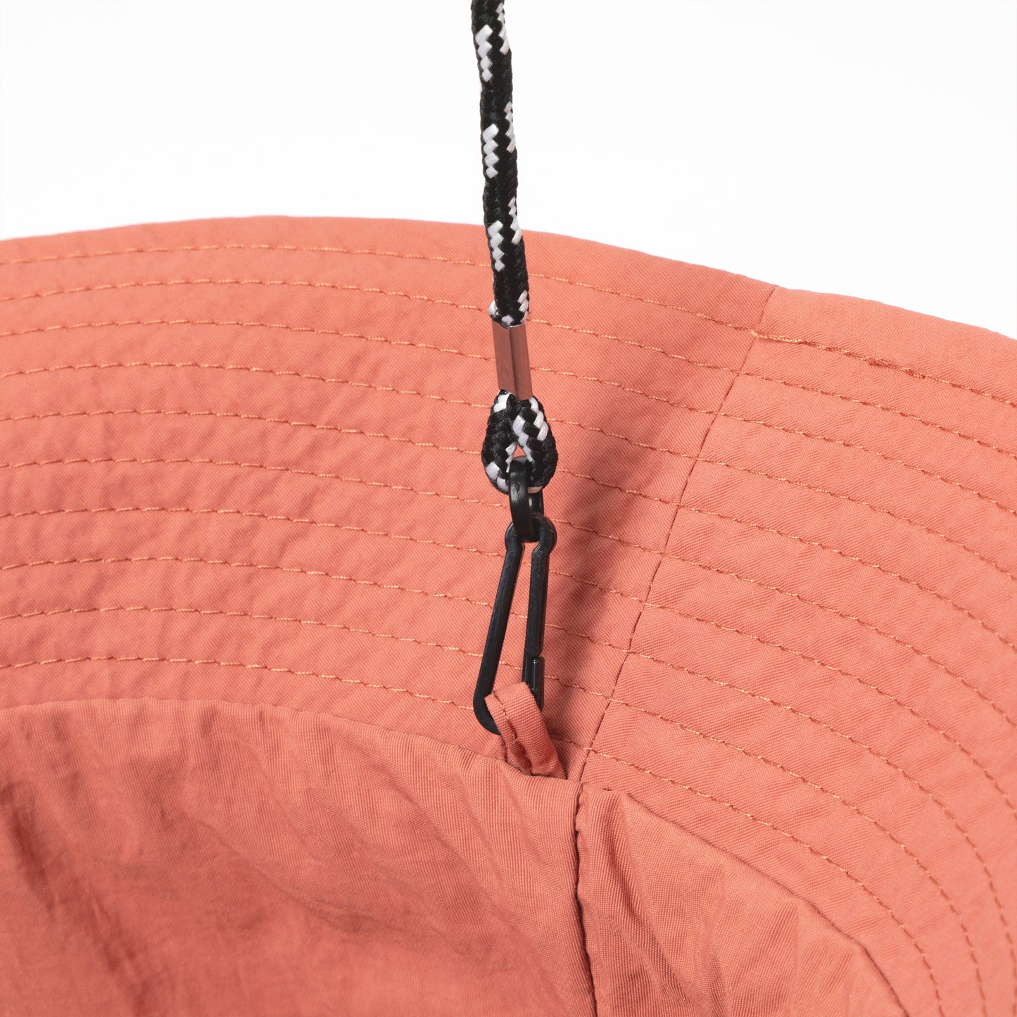 Close-up of a coral fabric bucket hat with a black adjustable tie on a white background