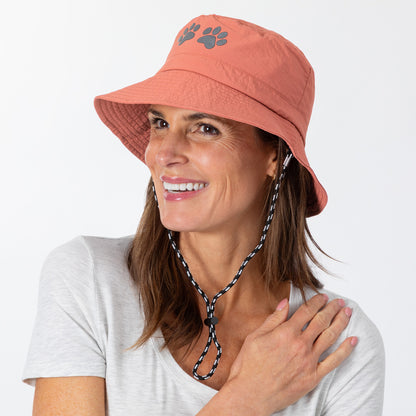 Woman wearing a coral bucket hat with a paw print design on a white background