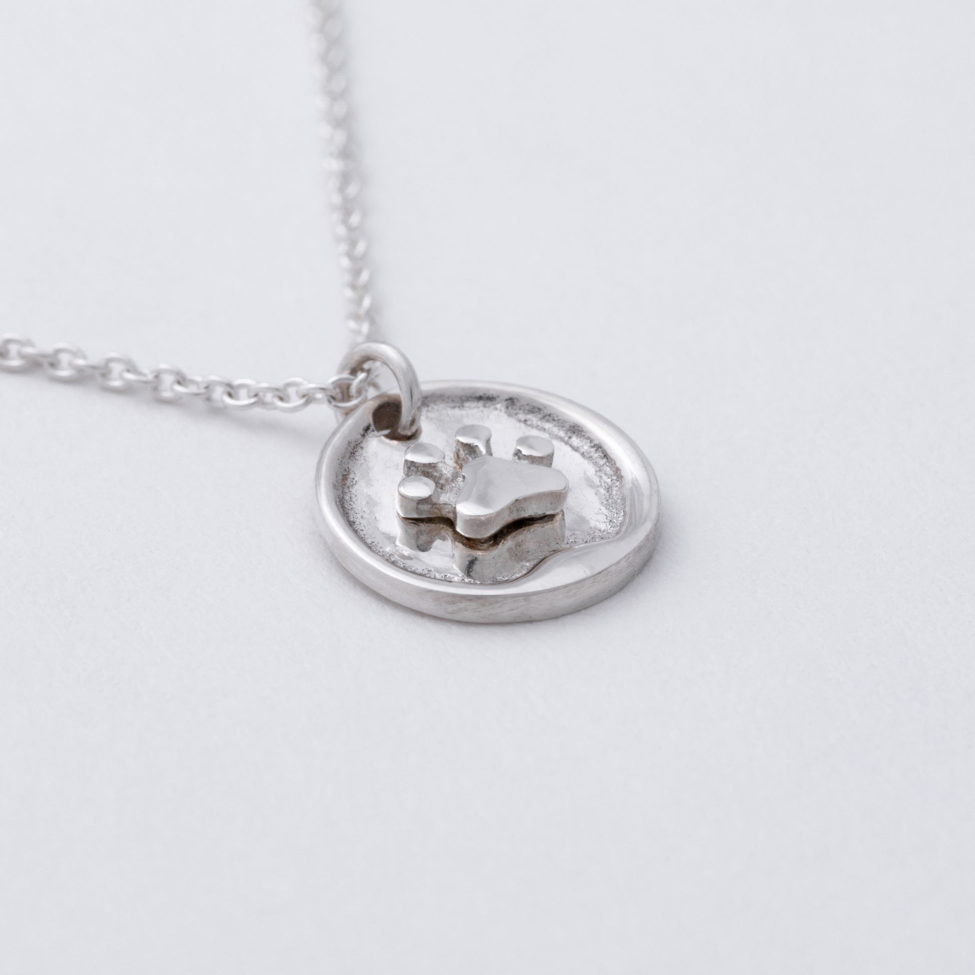 Sterling silver circular pendant with a small paw print on it, against a white background.