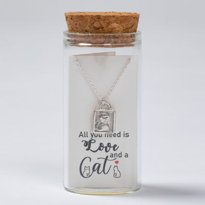 Glass jar with cork lid containing a necklace with a cat-themed pendant and text 'All you need is love and a cat'.