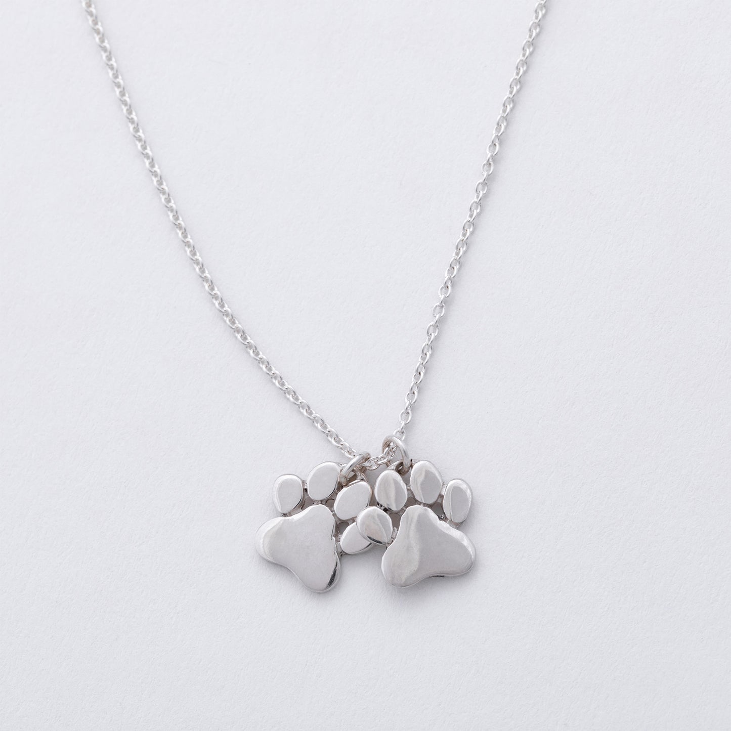Silver necklace with paw-shaped pendants on a light gray background
