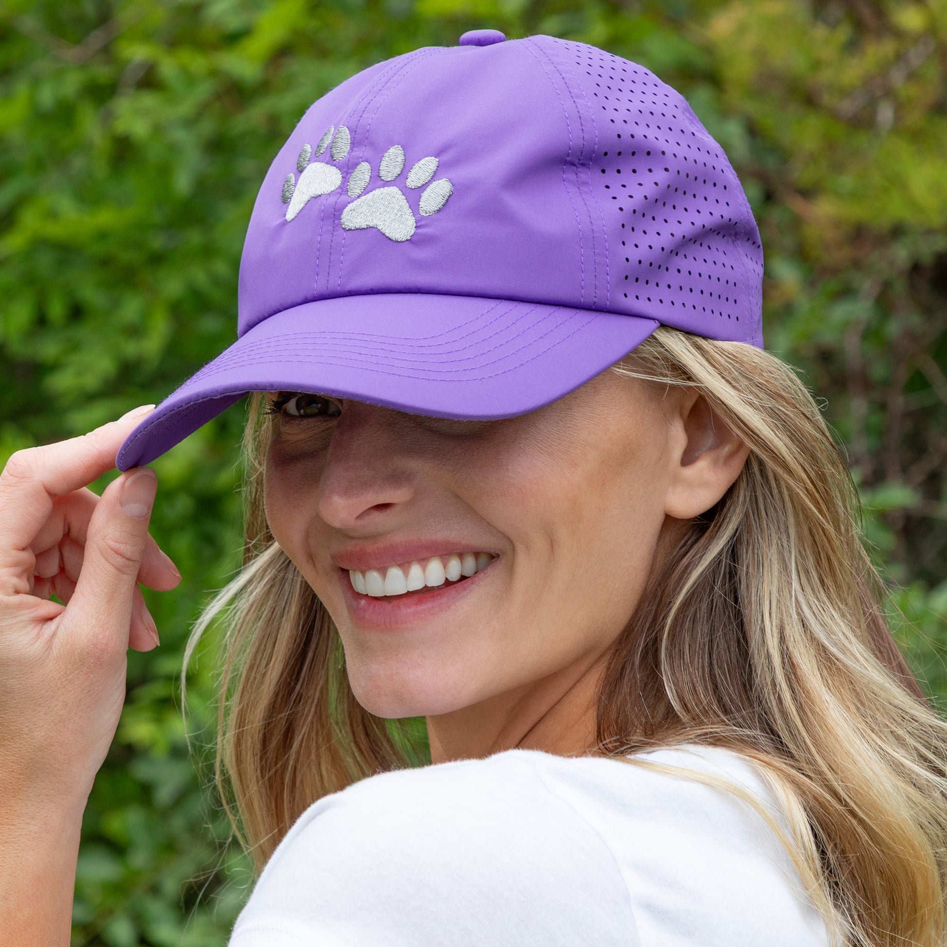Woman wearing purple cap with embroidered paws on the front, with greenery in the background.