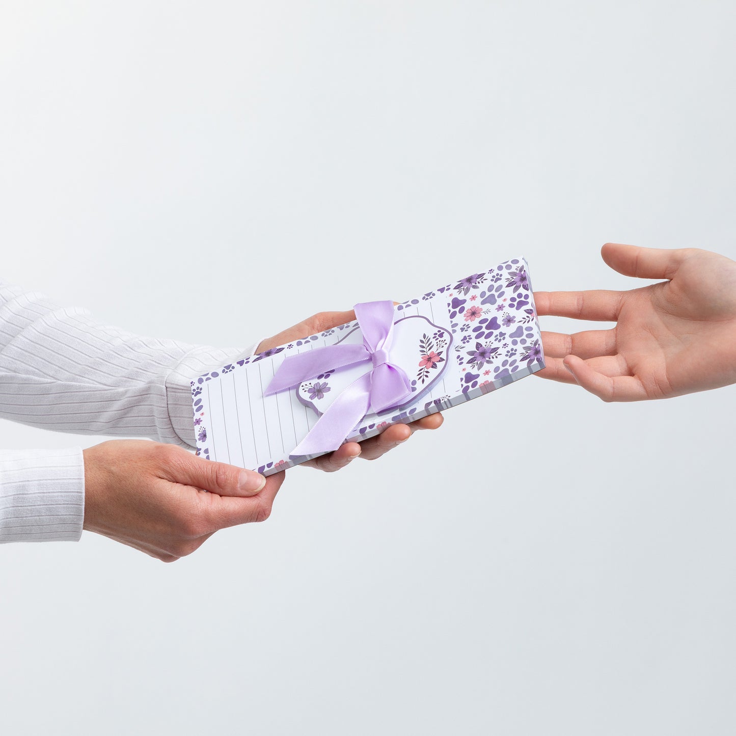 A person hands a note pad wrapped in floral paper with a ribbon.