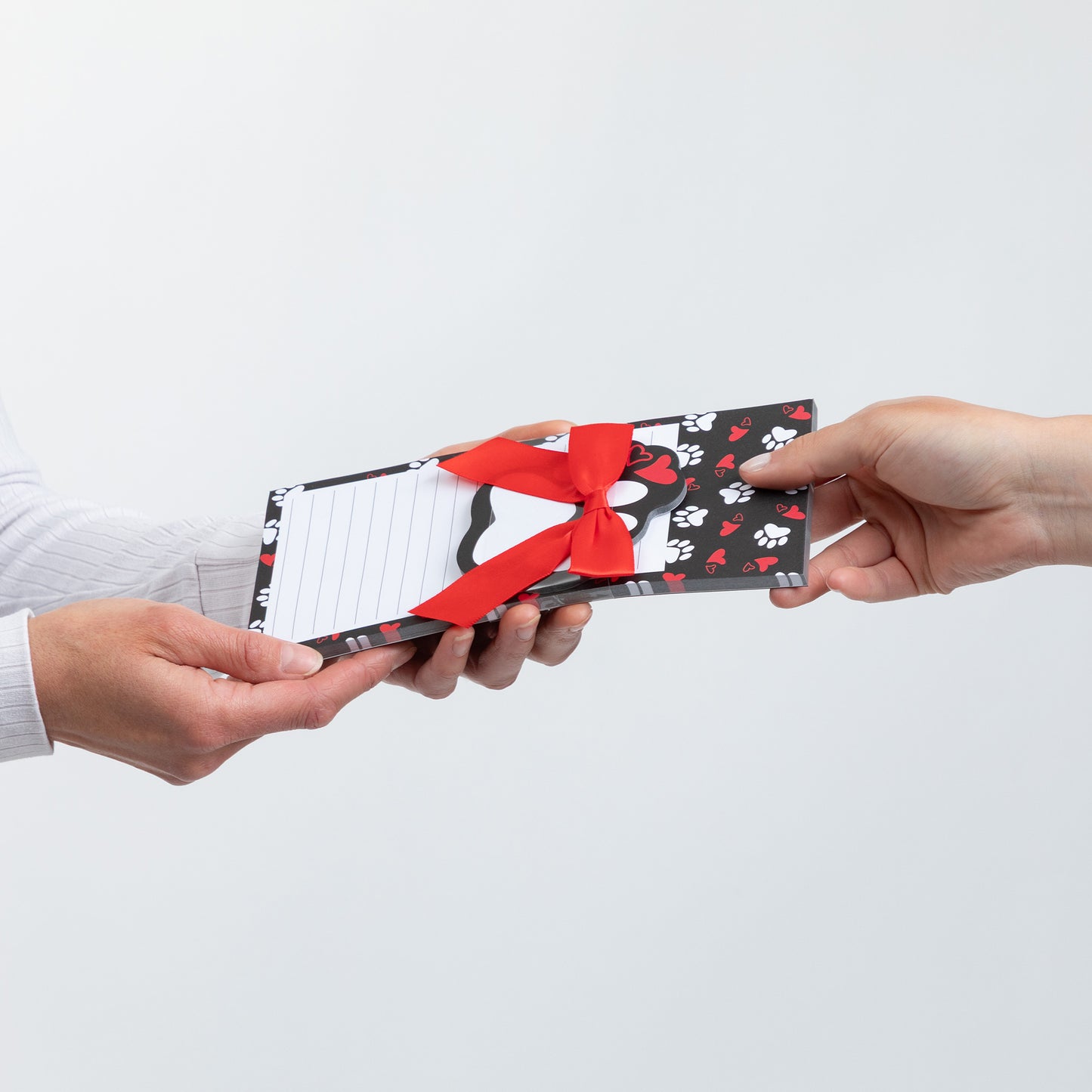 Hands exchanging a gift-wrapped notepad with a red ribbon on a white background.