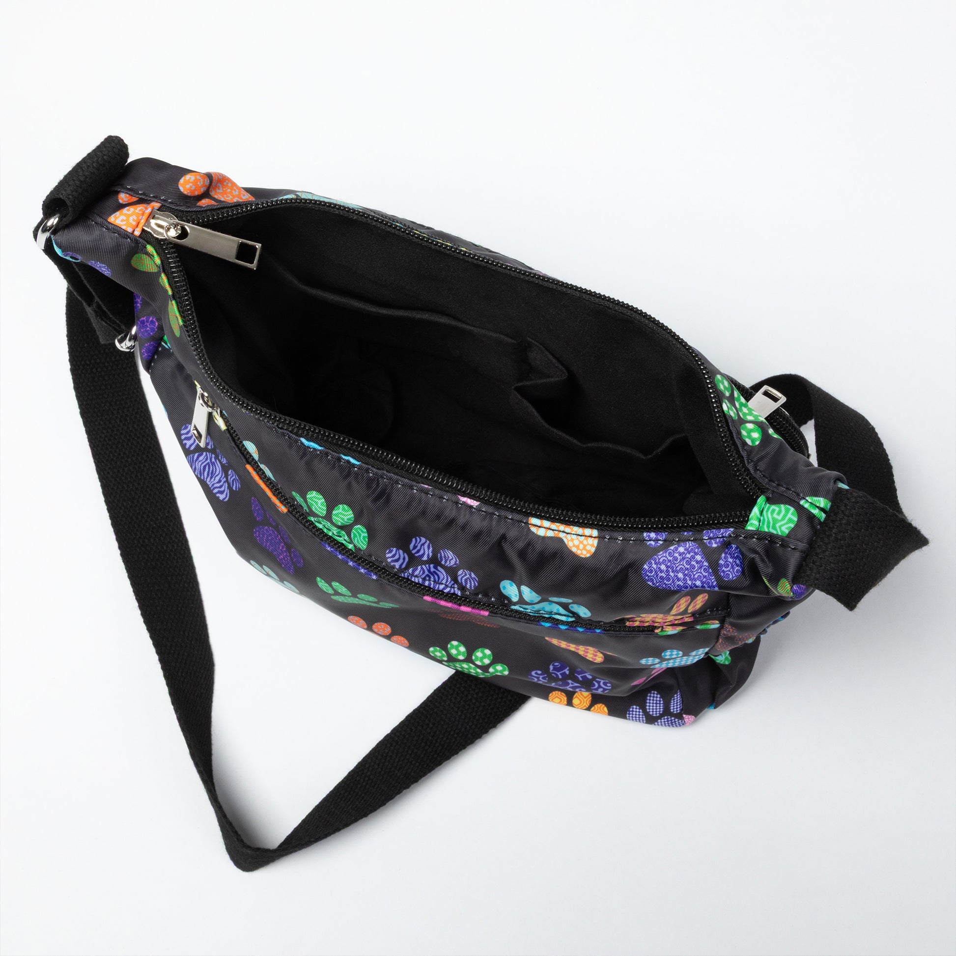 A black nylon crossbody bag with a colorful paw print pattern, shown open to reveal its interior compartments and black strap on a white background.