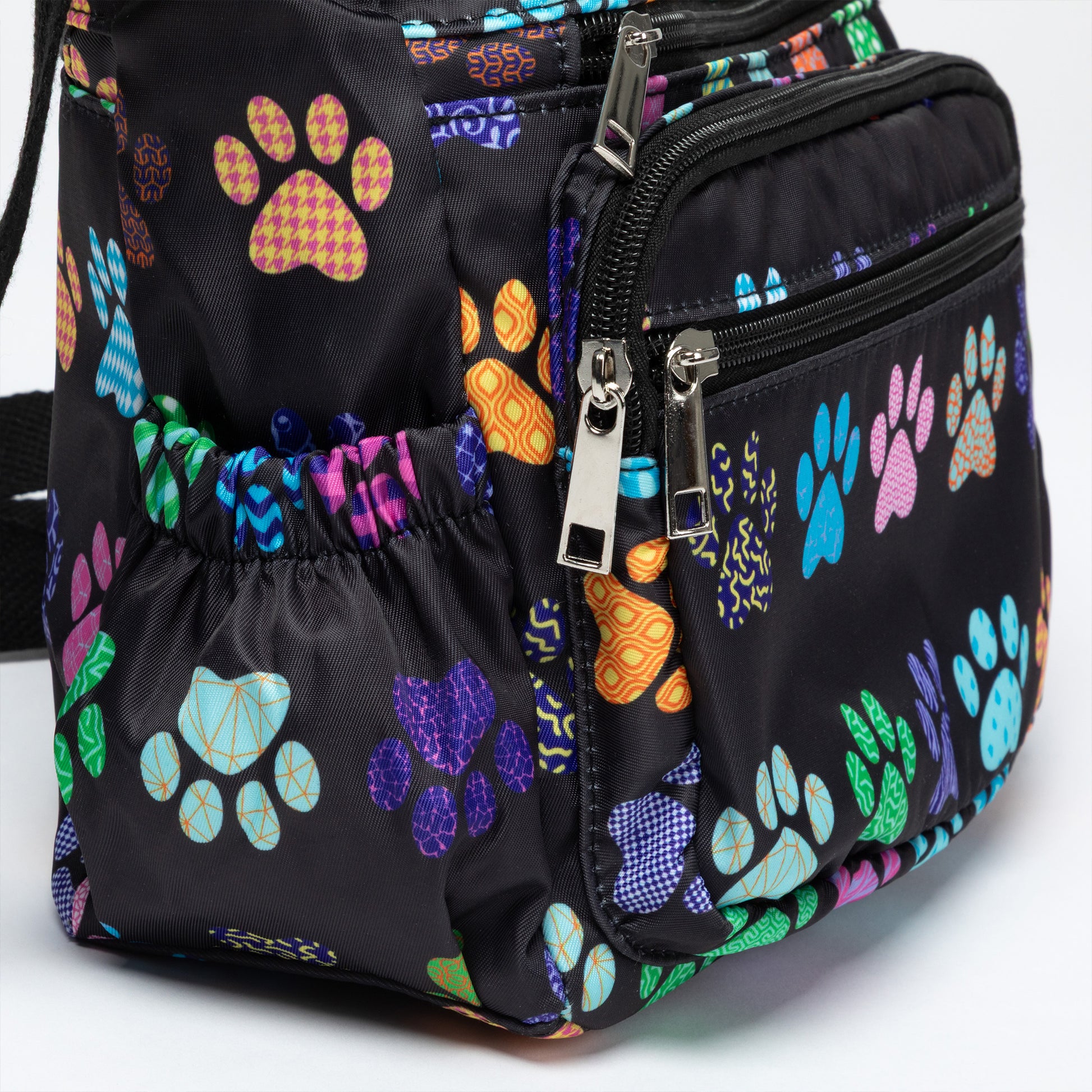 A black crossbody bag with a colorful paw print pattern, featuring a main zippered compartment, a front zippered pocket, and a side mesh pocket.