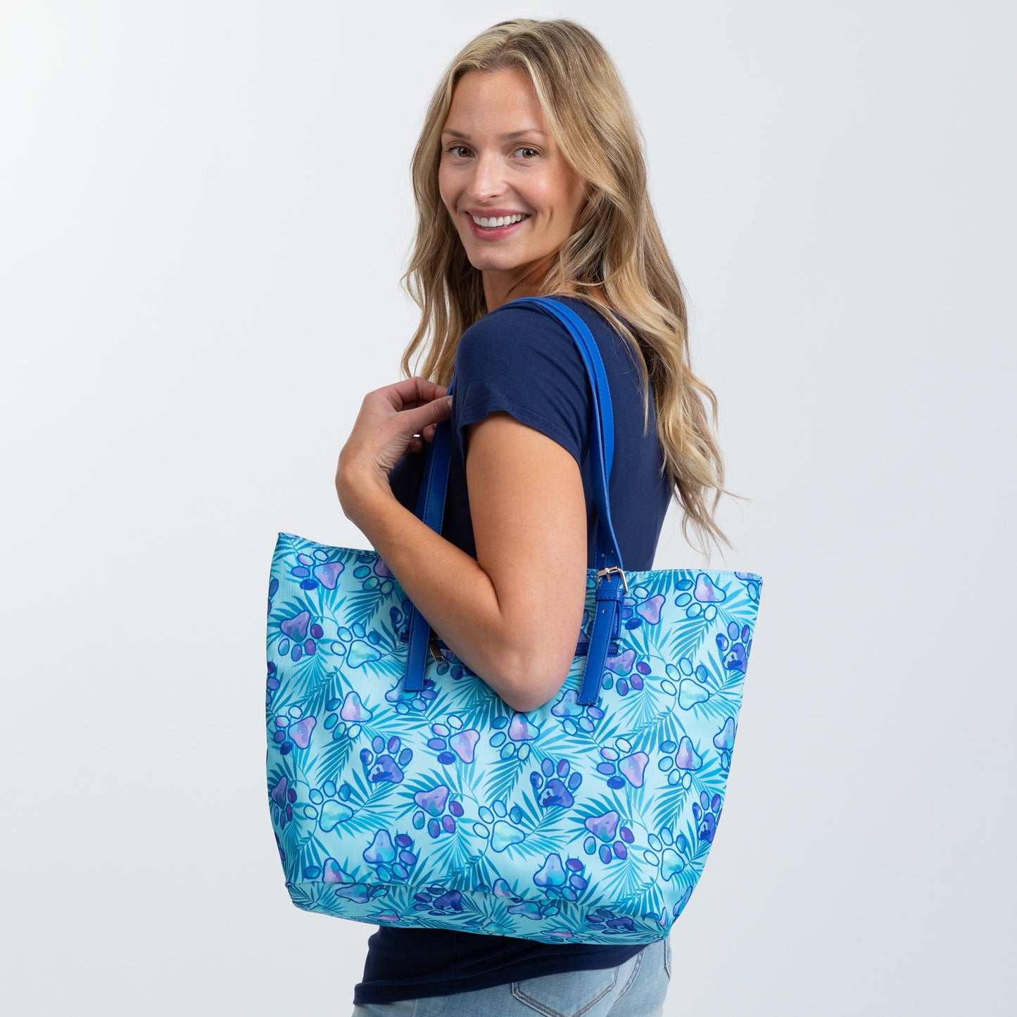 Smiling woman holding a blue floral tote bag, wearing a casual navy shirt.