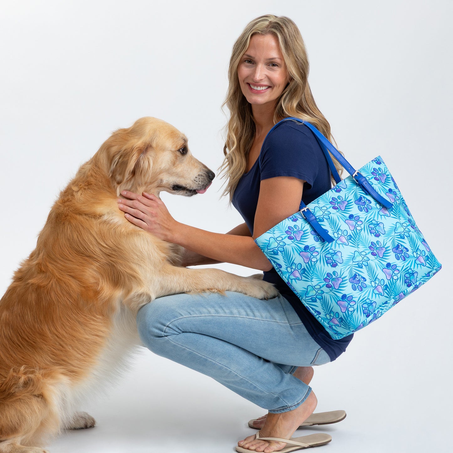 Smiling woman cuddles a golden retriever while holding a colorful tote bag.