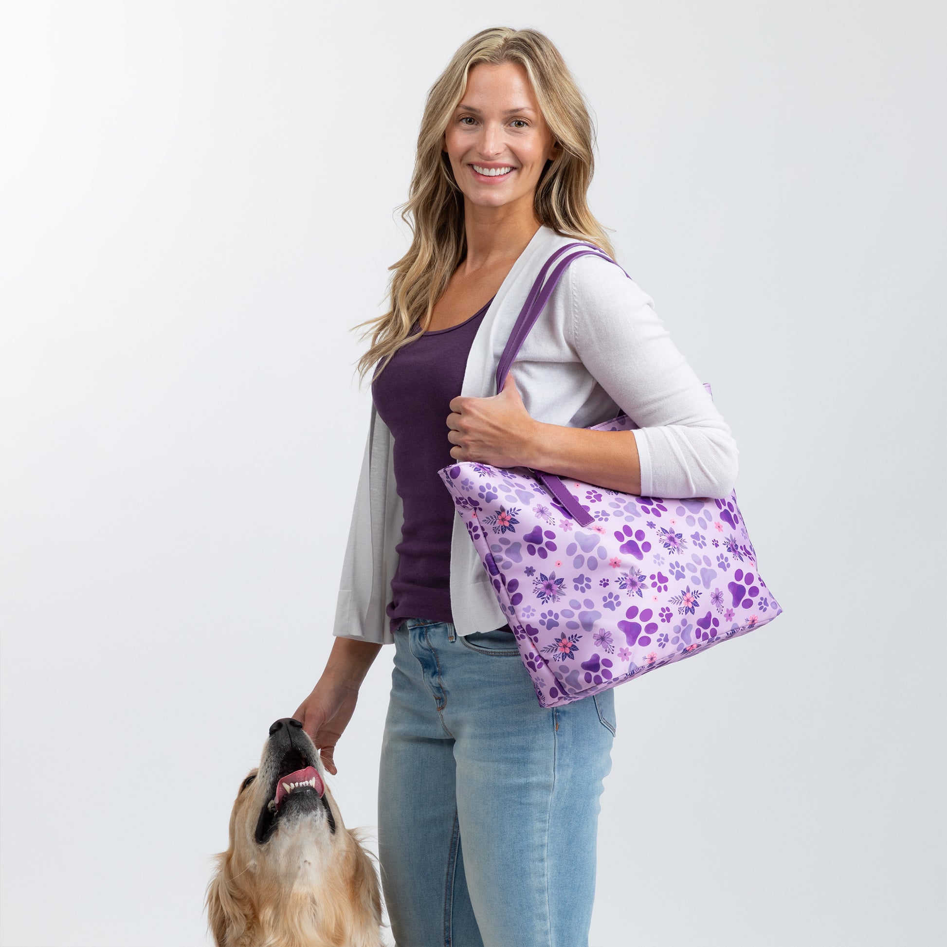 Smiling woman holds a purple pet-patterned bag with a golden retriever nearby.