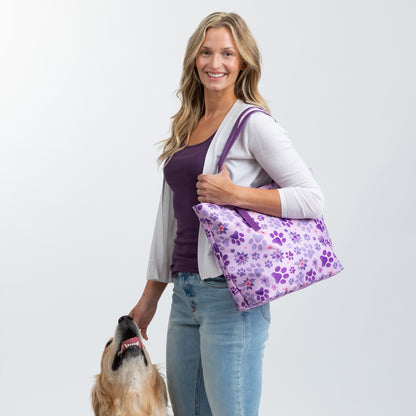 Smiling woman holds a purple pet-patterned bag with a golden retriever nearby.
