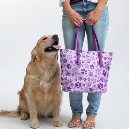 A person holds a purple floral tote bag beside a golden retriever.