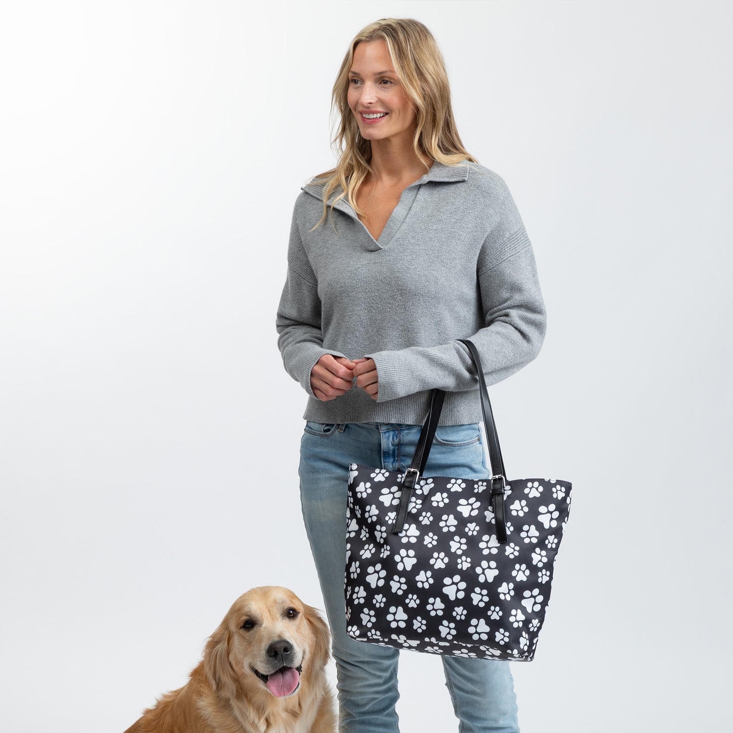 Person holding a paw-themed tote bag beside a golden retriever.