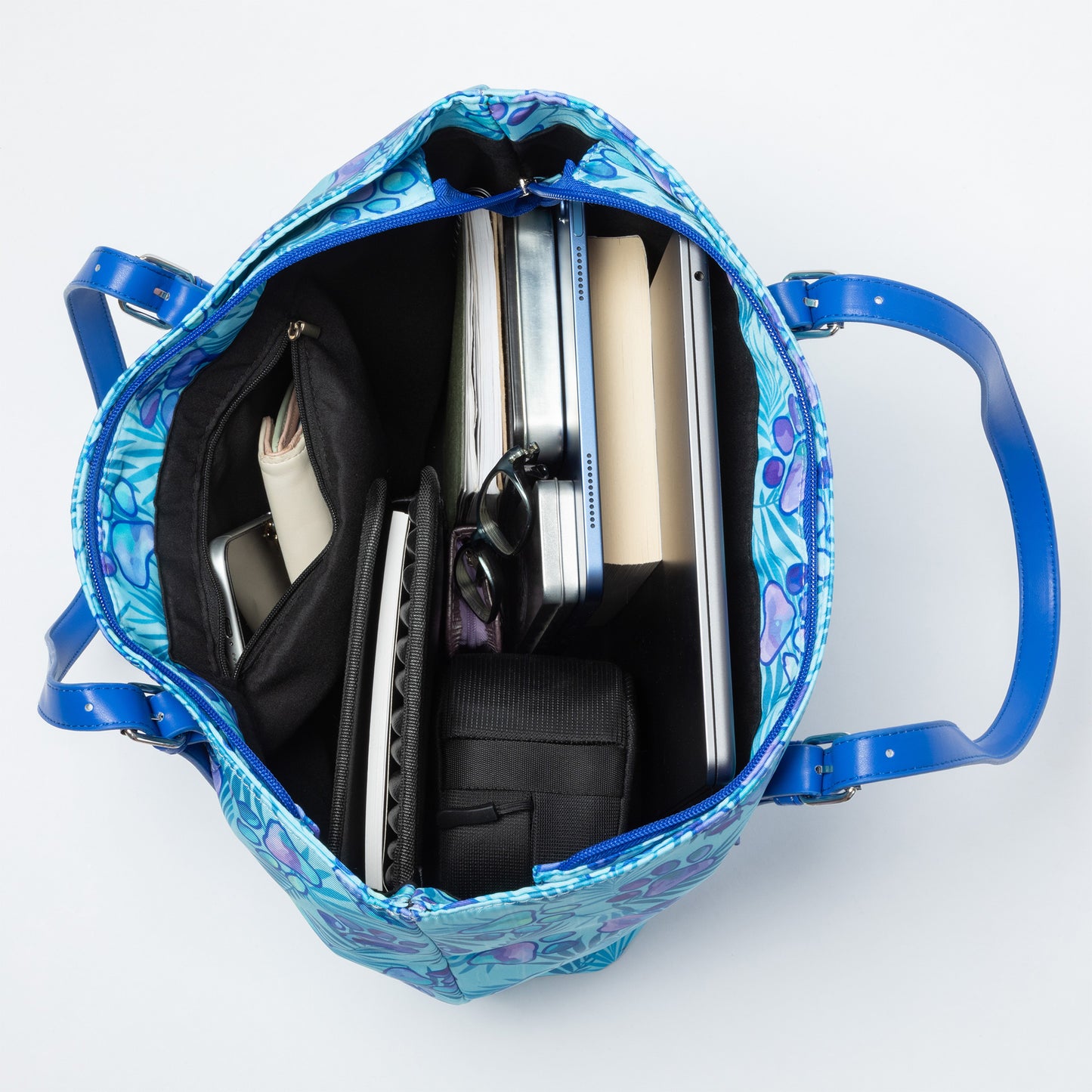 A paw print patterned tote bag filled with a laptop, tablet, wallet, books, and more against a white background.