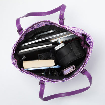 A purple paw printed tote sitting open against a white background, showing the pockets inside and holding books, laptop, tablet, sunglasses etc.