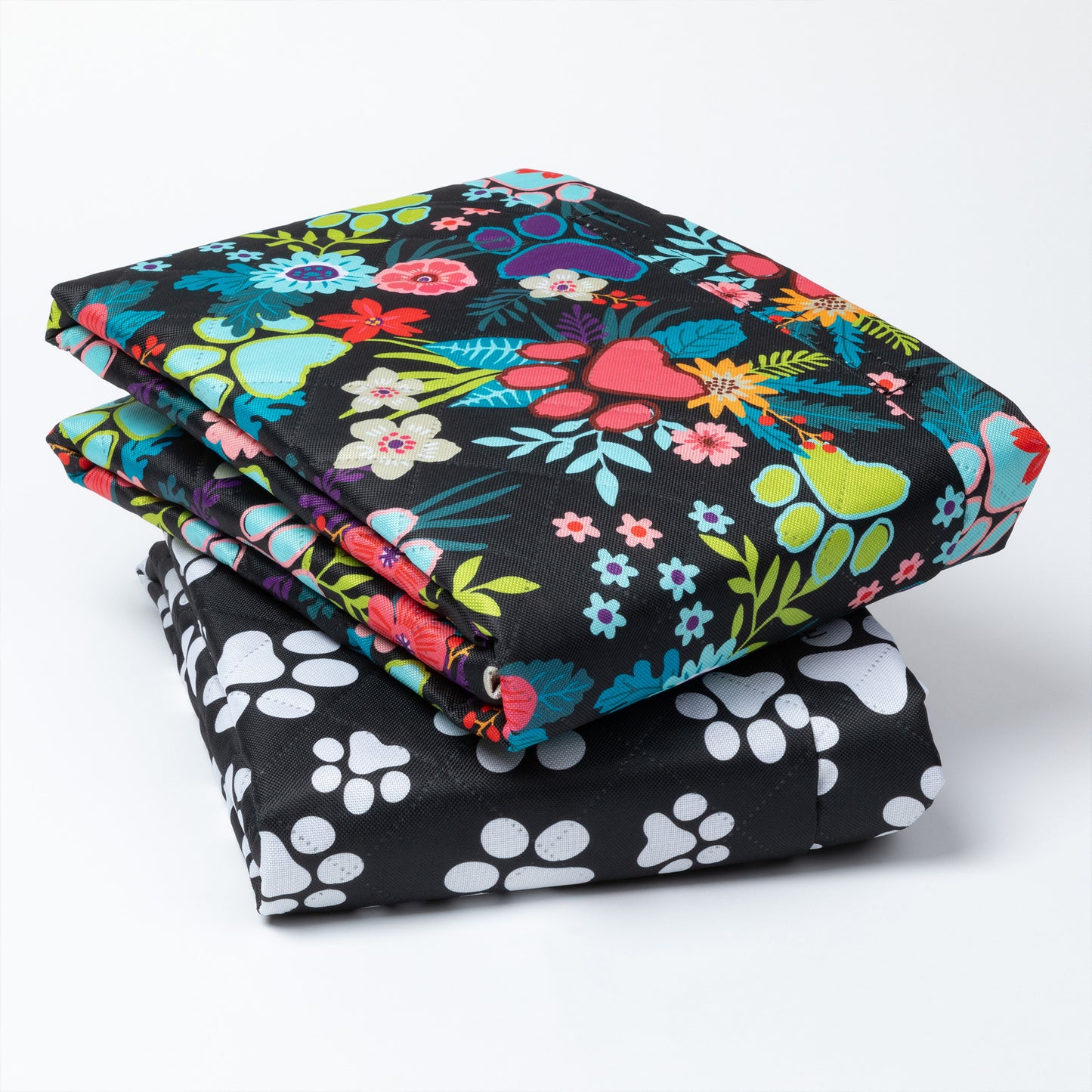 Stack of colorful floral-patterned fabric and black fabric with white paw prints on a white background